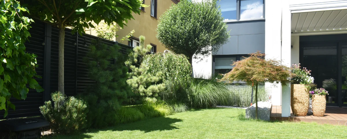 Widok na nowoczesny taras w ogrodzie minimalistycznym na Oporowie we Wrocławiu, otoczony roślinnością i trawnikiem.