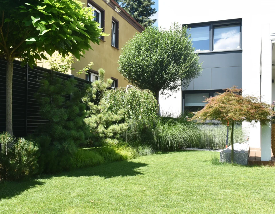 Widok na nowoczesny taras w ogrodzie minimalistycznym na Oporowie we Wrocławiu, otoczony roślinnością i trawnikiem.